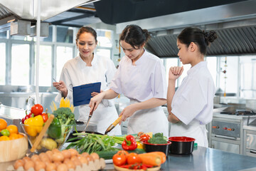 Young Chefs Learning to Cook with Fresh Ingredients, Culinary Instructor Guides Students in a Professional Kitchen, Women in Chef Uniforms Preparing Food in a Commercial Kitchen