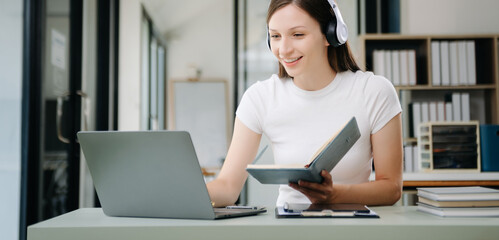 Obraz premium happy young student studying at the college library, sitting at the desk, using a laptop computer, tablet and headphones having a video chat.
