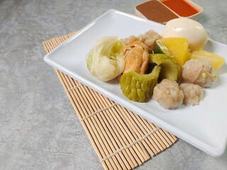 Siomay Bandung (Shumay) or steamed dumplings with boiled egg, tofu, potato, bitter melon and cabbage roll. Indonesian traditional street food with peanut sauce and chili sauce, served with green lime
