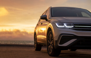 Silhouetted by a colorful sunset, a gray car stands near the ocean's edge. The warm light and open space capture a moment of solitude and exploration. 