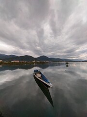 Serene lake landscape reflecting dramatic clouds with a solitary boat floating peacefully on the water