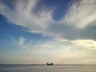 Lone sailboat drifts peacefully on the tranquil ocean under a serene, cloudy blue sky at dusk
