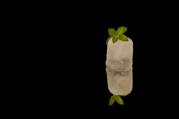 Ice cube with mint leaves reflecting on a black background, creating a refreshing and minimalist...