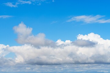 A beautiful skyscape with a bright blue sky and fluffy white cumulus clouds. The horizon features a...