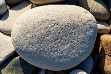 A smooth, large stone rests among smaller beach pebbles, with natural sunlight highlighting its...