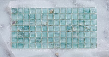 Rectangular mosaic tile sheet. Light blue glass squares with subtle variations, mounted on mesh backing. Marble surface visible around edges.
