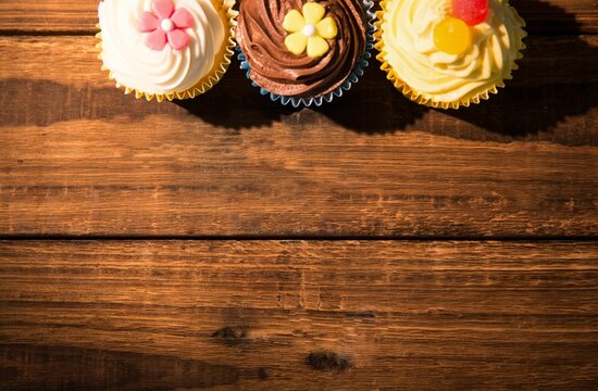 Fototapeta Three frosted cupcakes are resting on wood grain table in flat design with fondant flowers, gummies
