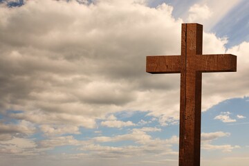 Flat design wooden cross is standing against cloudy cumulus sky, showing weathered grain texture