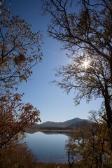 Flat design serene lake and distant hills are reflecting calm sky with sunburst amid russet leaves