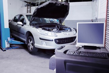Flat design silver sedan is being lifted on hydraulic lift with hood open and diagnostic cart