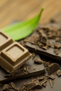 Fototapeta milk chocolate square is resting on dark chocolate fragments beside green leaf in macro photography