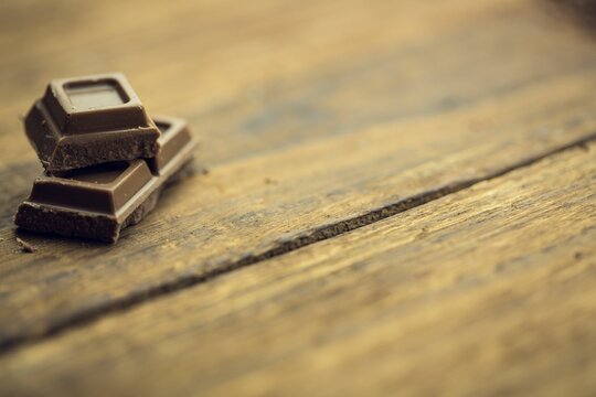 Naklejki Chocolate squares are resting on rustic wooden plank surface with grain knots in 3D render