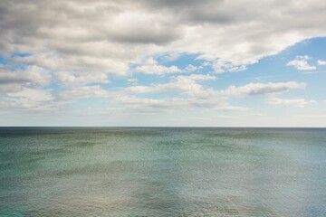 Calm ocean surface is being shown with horizon line in flat design and scattered clouds