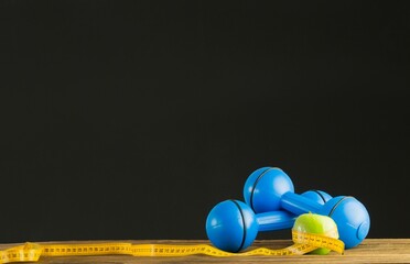 Blue dumbbells with green apple and measuring tape