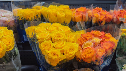 Bouquets of yellow and orange roses wrapped in clear plastic on display.