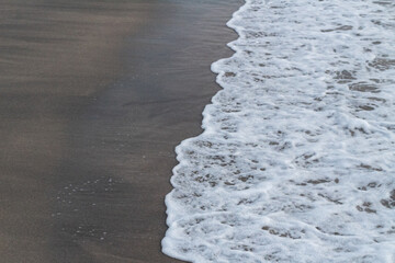 Close-up view of textured white ocean foam meeting dark brown sand