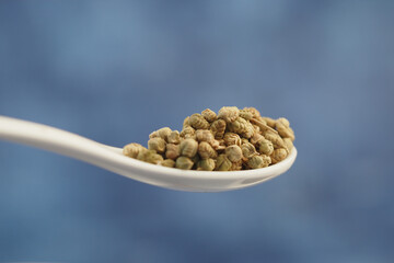 Spoonful of tiny green seeds against a blue background