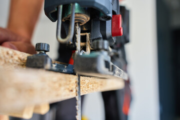Close up of electrical handheld jigsaw cutting wooden board in workshop. Work tools for manual labor. Carpentry and woodworking concept