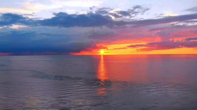 Vibrant sunset with fiery orange and red hues reflecting a brilliant path on the sea, beneath dark, dramatic clouds. Powerful and beautiful seascape.