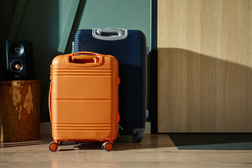 Two modern suitcases, orange and navy, stand near entrance door in morning light. Packed luggage in...