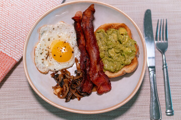 Hearty breakfast plate with crispy bacon, fried egg, sautéed mushrooms, and creamy avocado toast on rustic ceramic dish—perfect for brunch menus, food blogs, or nutrition features.
