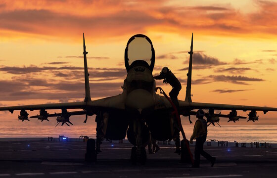 Fighter jet front view silhouette on aircraft carrier at sunset