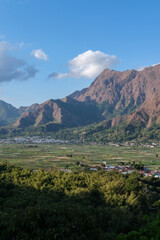Obraz premium Beautiful rice fields stretch across the valley with the striking Anak Dara Hill of Sembalun – Lombok rising in the background under a bright blue sky.