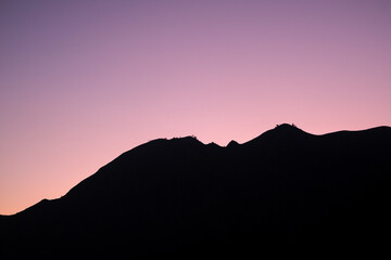 Glowing twilight sky blankets the rolling hills of Sembalun, Lombok, painting the horizon in soft purples and oranges as mountain silhouettes fade into serene dusk.