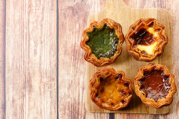 Stack of assorted Portuguese sweet dessert egg tart or Pastel de Nata on wooden board on wooden...