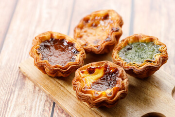 Stack of assorted Portuguese sweet dessert egg tart or Pastel de Nata on wooden board on wooden table.