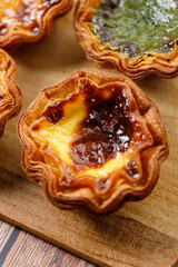 Stack of assorted Portuguese sweet dessert egg tart or Pastel de Nata on wooden board on wooden table.