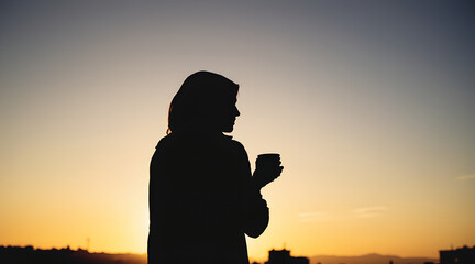 Silhouette of Woman Drinking Coffee at Sunset with City Skyline
