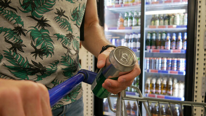 Close-up of male customer's hand putting a cold beer can in a shopping cart