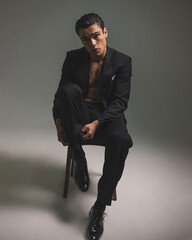 cool fashion guy in tuxedo with no shirt adjusting socks while sitting