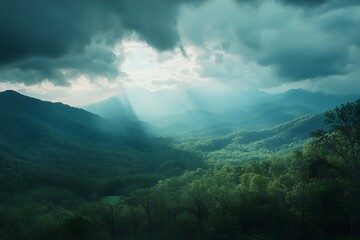 A panoramic view of the Mountains, with rays piercing through the clouds above, surrounded by lush greenery and forest-covered hills below. 