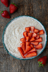 Oatmeal porridge with fresh strawberries in a plate on a wooden table
