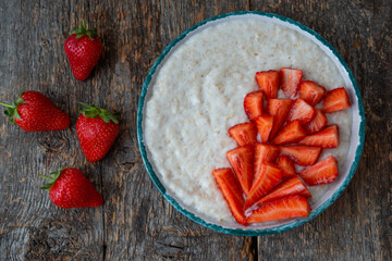 Oatmeal porridge with fresh strawberries in a plate on a wooden table