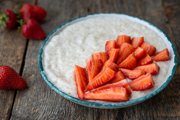 Oatmeal porridge with fresh strawberries in a plate on a wooden table