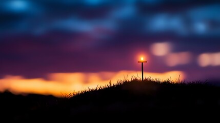Silhouette of wooden cross on grassy hill against dramatic sunset sky with glowing orange clouds and deep blue atmosphere, spiritual nature background.