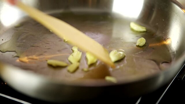 Sliced garlic in olive oil in stainless steel pan