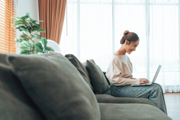 Young Asian beautiful woman relaxing on comfortable couch, using laptop at home, happy girl chatting with friends in social network, spending weekend, watching movie, shopping online