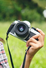 Vertical Asian Women with vintage film camera take a photo. Smiling female photographer look at photo from professional camera outdoor. Vertical photo of young woman shoot photo in green nature park