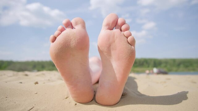 Woman legs barefoot relaxing lying on sandy beach on back, close up on feet