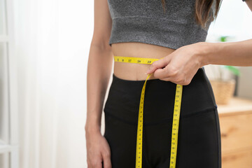 Weight lose, loss concept. Slim body asian young woman hand use tape measuring around waistline in...