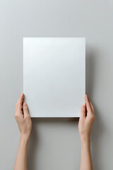Female hands holding blank white paper sheet against neutral gray background, mockup for presentation or design placement.