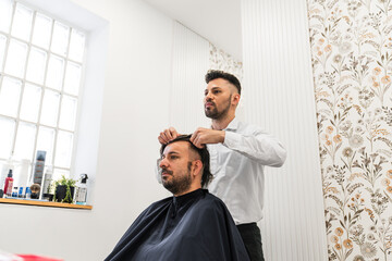 Hairdresser carefully placing hair replacement system on head of male client in hair salon, providing solution for hair loss