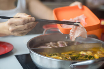 Close-up of a woman putting food in a shabu-shabu pot