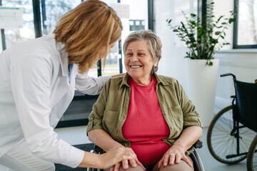 Geriatric doctor talking with patient in a wheelchair in hospital hallway.