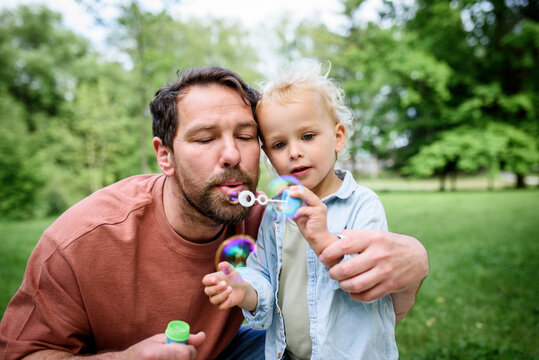 Father and son blowing soap bubbles in park. - Powered by Adobe