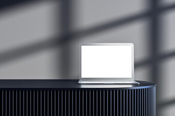 Laptop with blank screen placed on dark modern podium in stylish interior studio with soft shadow...